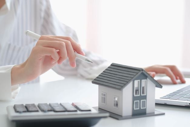 Woman at table doing paperwork with calculator and home model