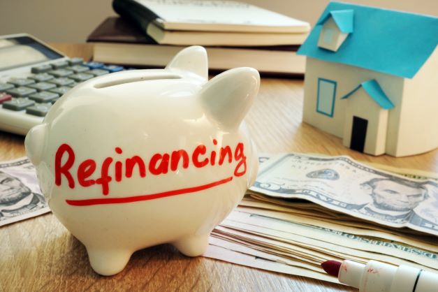Piggy bank next to money and house model with 'refinancing' written on it