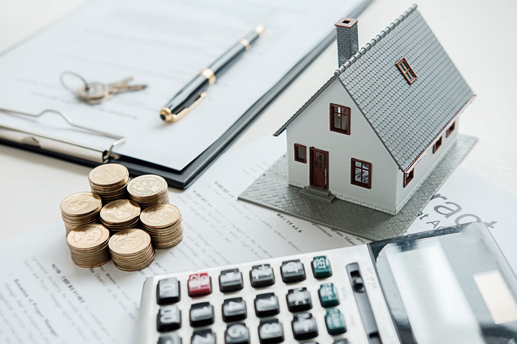Small house figure next to stacked coins, a calculator, and papers