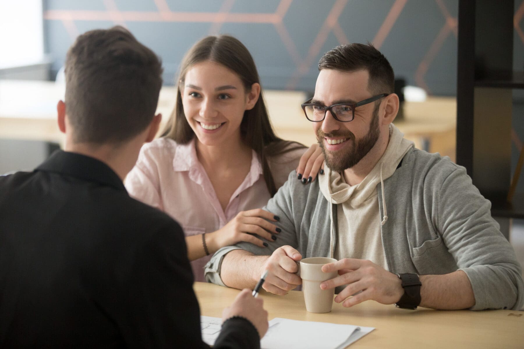Couples in meeting with banker smiling and sitting down, hands on table.